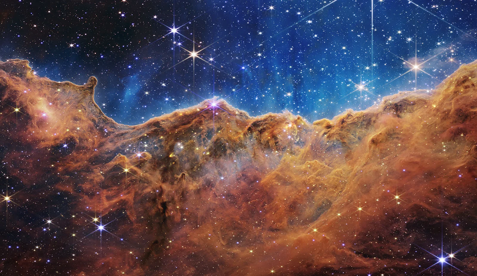 Amber cliffs of gas and dust beneath a blue star field in the Carina Nebula